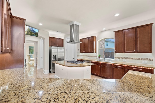 kitchen featuring appliances with stainless steel finishes, island exhaust hood, light stone counters, and a sink