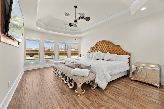 bedroom with crown molding, a raised ceiling, visible vents, light wood-type flooring, and baseboards