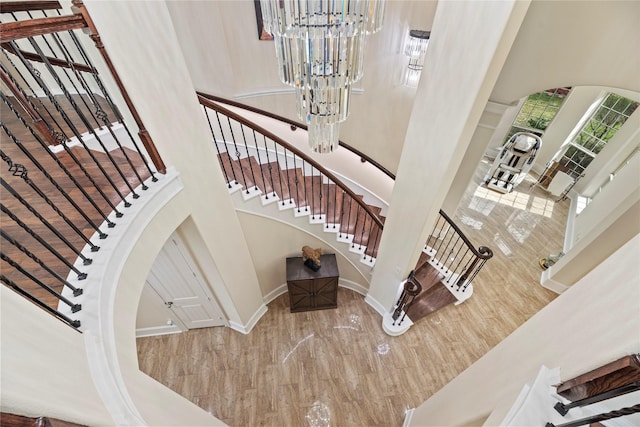 stairs featuring arched walkways, a towering ceiling, baseboards, and an inviting chandelier