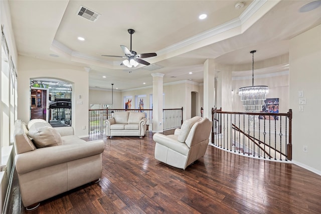 living area featuring visible vents, dark wood-style floors, ornamental molding, a tray ceiling, and ornate columns