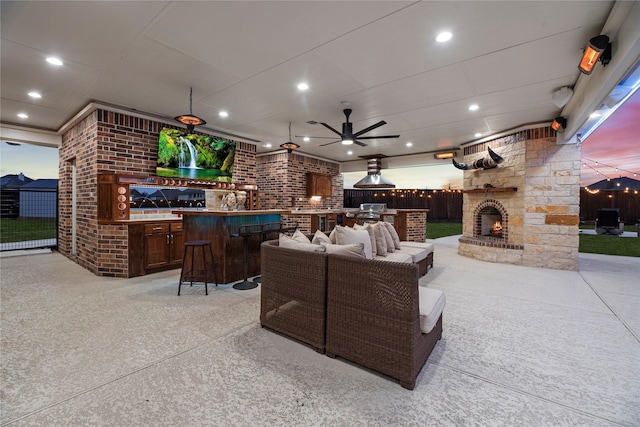 view of patio featuring an outdoor kitchen, an outdoor living space with a fireplace, fence, a ceiling fan, and a bar