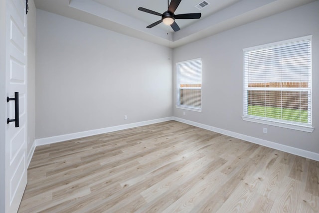 spare room with light wood finished floors, baseboards, and a raised ceiling