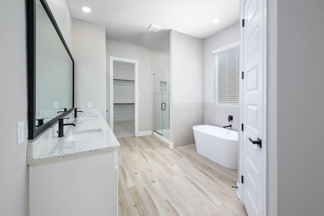 bathroom featuring double vanity, wood finished floors, a sink, a shower stall, and tile walls