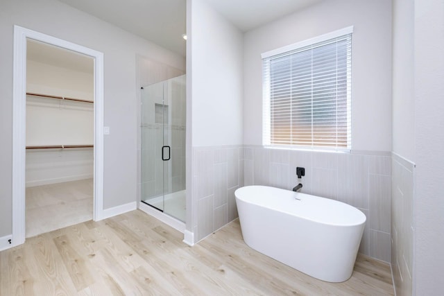 bathroom with a stall shower, wainscoting, wood finished floors, a freestanding bath, and tile walls