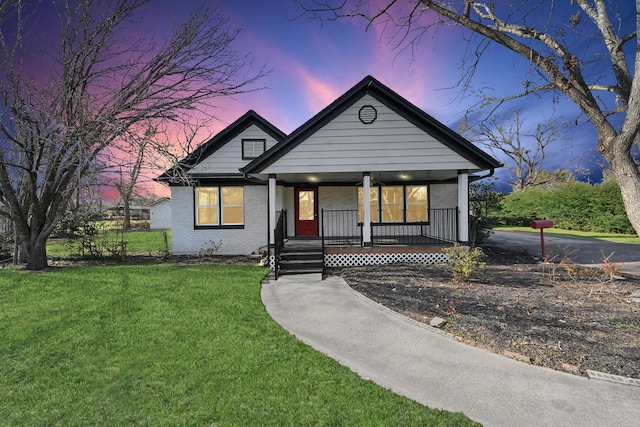 bungalow with a porch, brick siding, and a lawn