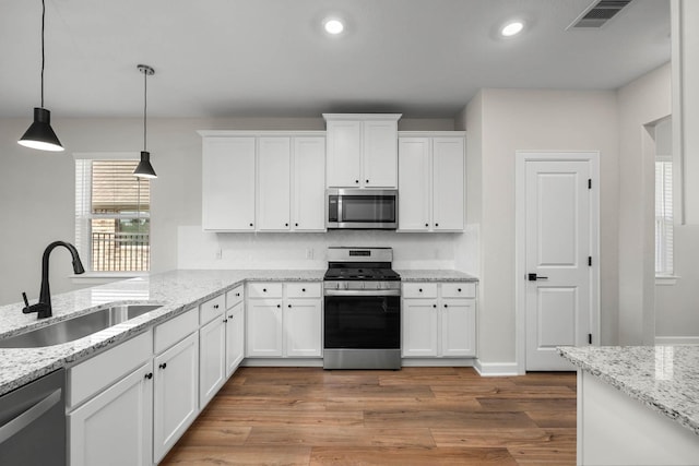 kitchen featuring hanging light fixtures, appliances with stainless steel finishes, a sink, and white cabinetry