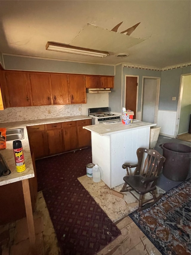 kitchen with brown cabinets, gas range gas stove, light countertops, under cabinet range hood, and a sink