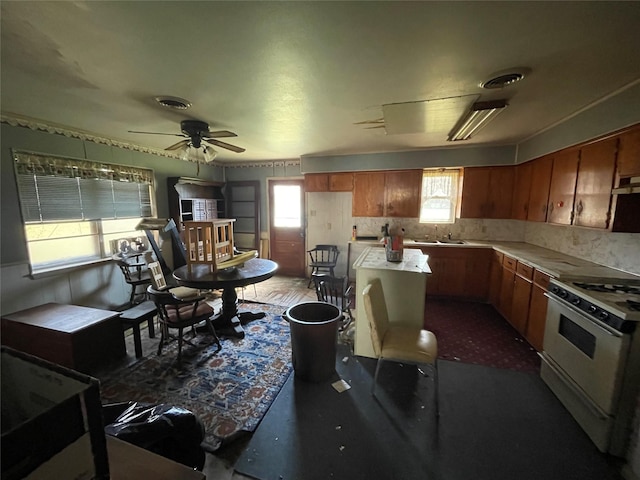 kitchen with gas range gas stove, light countertops, brown cabinetry, a sink, and ceiling fan