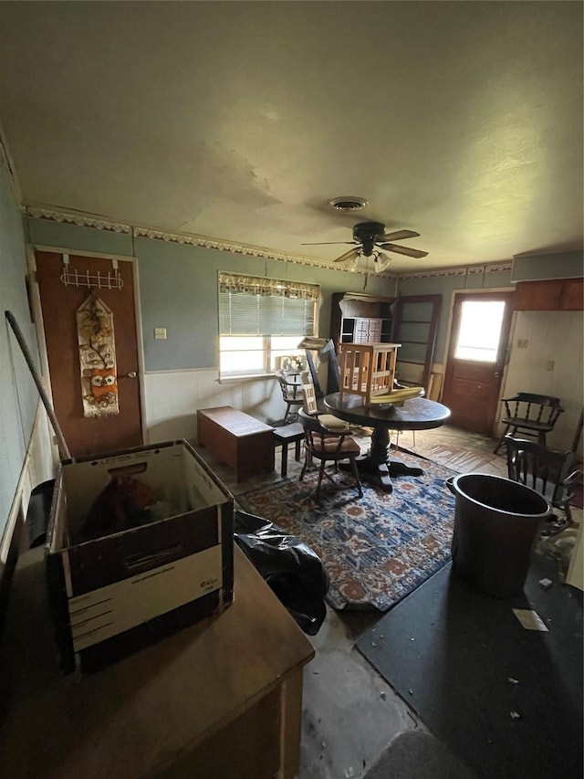 interior space with a wainscoted wall, ceiling fan, visible vents, and unfinished concrete flooring