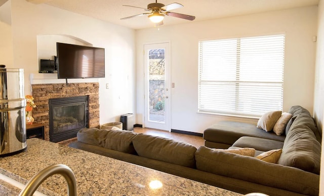 living area featuring ceiling fan, baseboards, and a stone fireplace