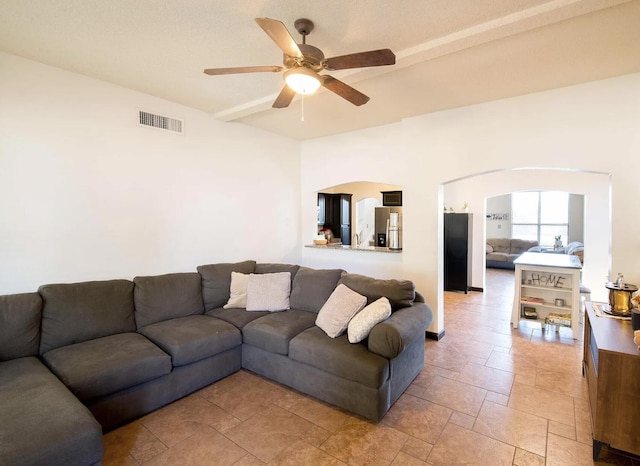 living room with arched walkways, ceiling fan, stone finish floor, and visible vents