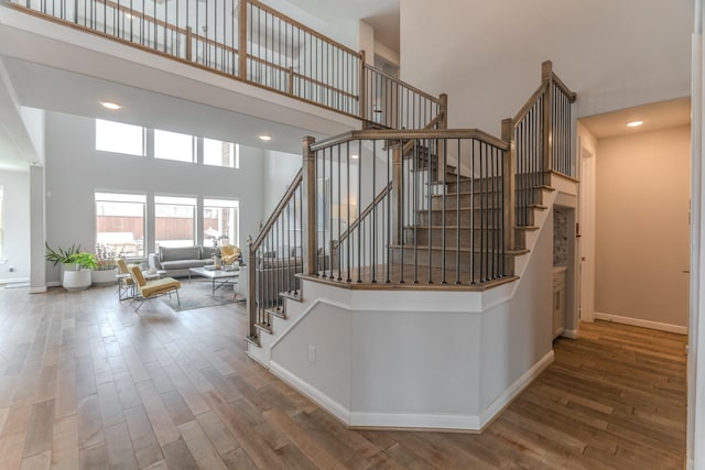 stairway with wood finished floors, a towering ceiling, and baseboards