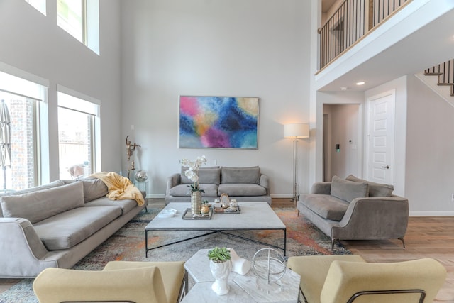 living area featuring a towering ceiling, stairs, baseboards, and wood finished floors