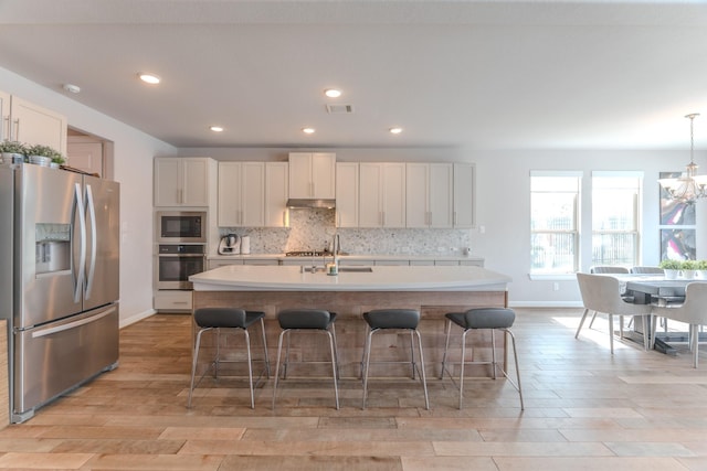 kitchen featuring light countertops, appliances with stainless steel finishes, a breakfast bar area, and a center island with sink