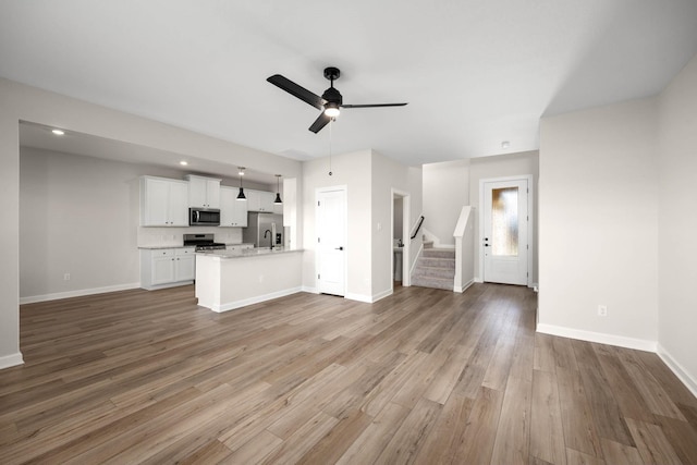 unfurnished living room with a ceiling fan, a sink, wood finished floors, baseboards, and stairs