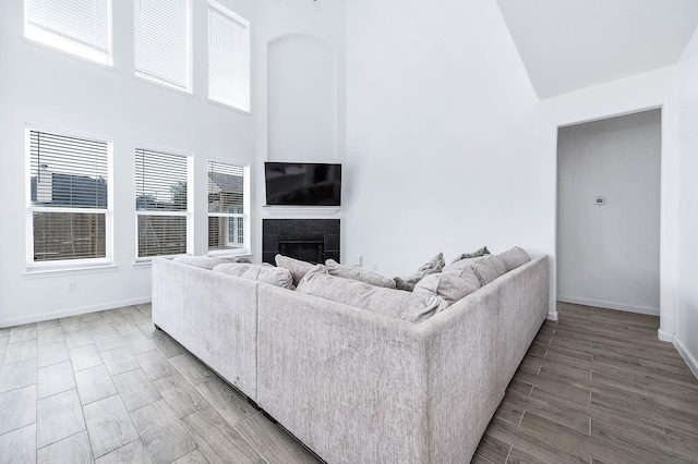 living area with a towering ceiling, wood tiled floor, baseboards, and a tile fireplace