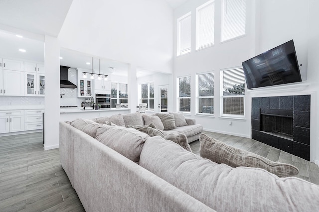 living area featuring a tile fireplace, recessed lighting, a towering ceiling, baseboards, and light wood-type flooring