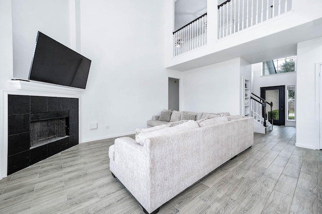 living area with light wood finished floors, stairway, a high ceiling, a tiled fireplace, and baseboards