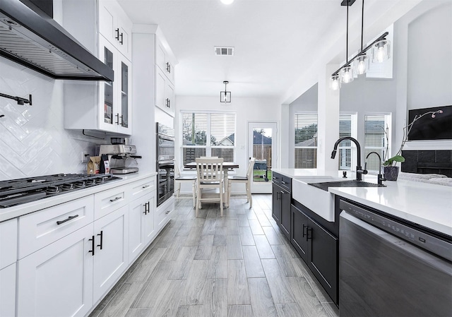 kitchen featuring white cabinets, wall chimney exhaust hood, appliances with stainless steel finishes, hanging light fixtures, and light countertops