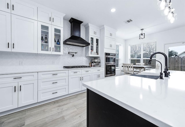 kitchen with decorative light fixtures, stainless steel appliances, light countertops, visible vents, and wall chimney exhaust hood