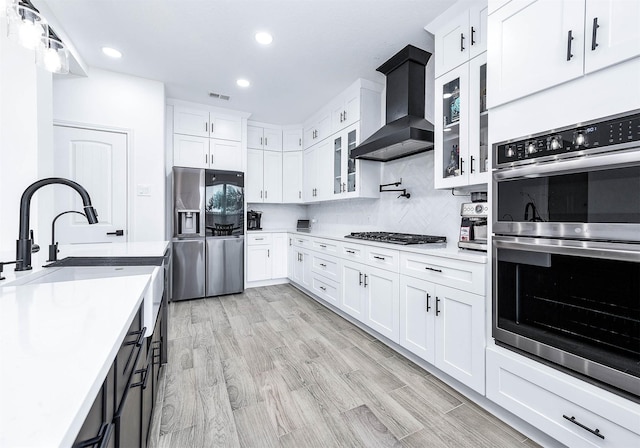 kitchen featuring light countertops, wall chimney range hood, appliances with stainless steel finishes, and white cabinetry