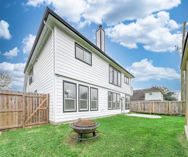 rear view of property with a fire pit, a yard, a chimney, and fence