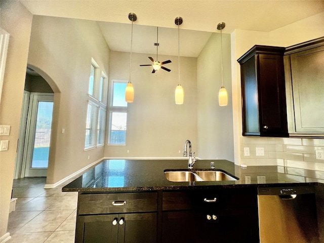 kitchen with dark stone counters, dark brown cabinets, stainless steel dishwasher, and a sink