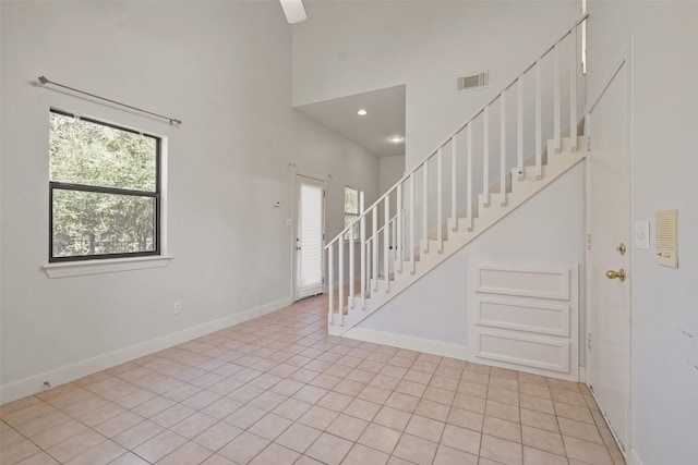 interior space with light tile patterned floors, visible vents, a high ceiling, baseboards, and stairs