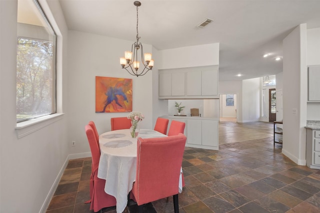 dining space featuring baseboards, stone finish flooring, visible vents, and a notable chandelier