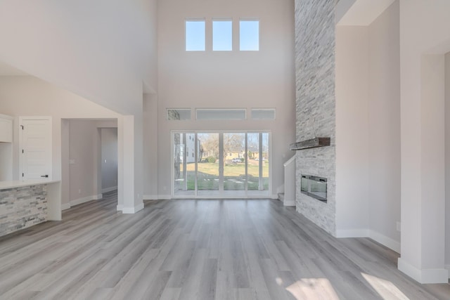 unfurnished living room with a stone fireplace, light wood-type flooring, a high ceiling, and baseboards