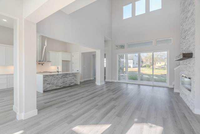 unfurnished living room with a high ceiling, a fireplace, light wood-style flooring, and baseboards