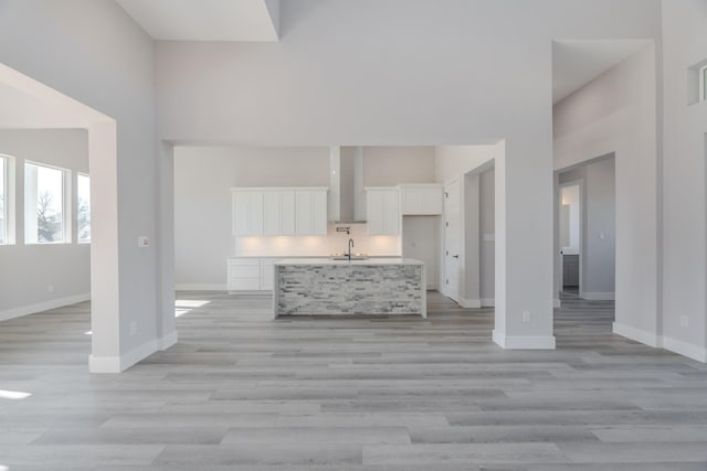 unfurnished living room featuring a sink, a towering ceiling, baseboards, and light wood finished floors