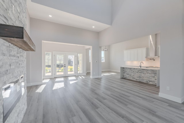 unfurnished living room featuring light wood finished floors, baseboards, a towering ceiling, french doors, and recessed lighting