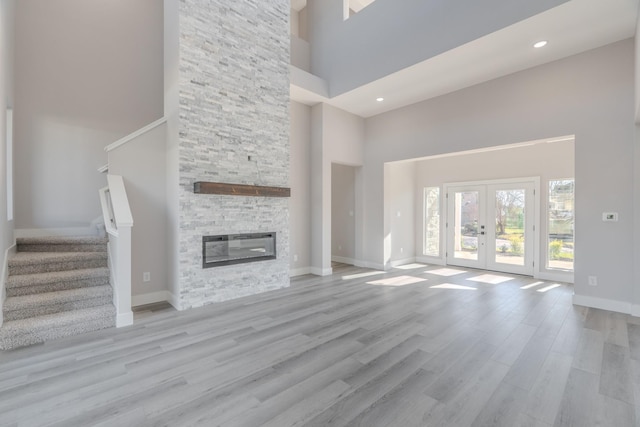 unfurnished living room with a fireplace, a towering ceiling, stairs, french doors, and light wood-type flooring