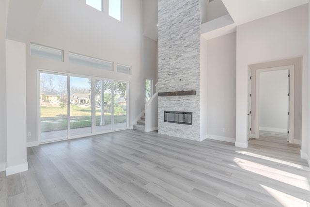 unfurnished living room with a fireplace, a towering ceiling, light wood-style flooring, and baseboards