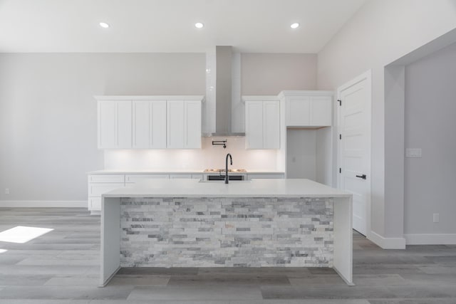 kitchen with light countertops, white cabinetry, a sink, an island with sink, and baseboards