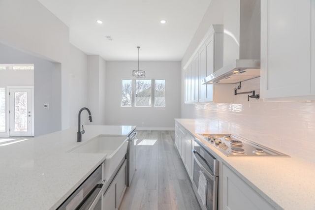 kitchen with decorative backsplash, wall chimney exhaust hood, stainless steel appliances, white cabinetry, and pendant lighting