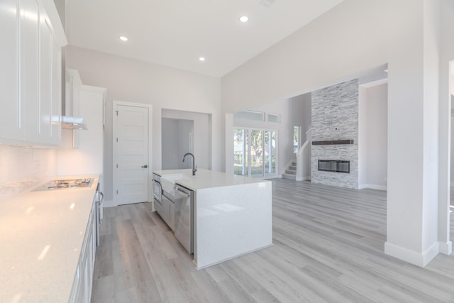 kitchen with a fireplace, white gas stovetop, stainless steel dishwasher, white cabinetry, and an island with sink