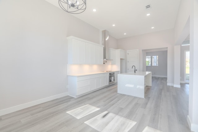 kitchen with white cabinets, oven, a kitchen island with sink, light countertops, and backsplash