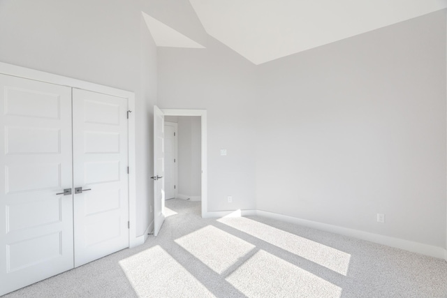 unfurnished bedroom with high vaulted ceiling, a closet, light carpet, and baseboards