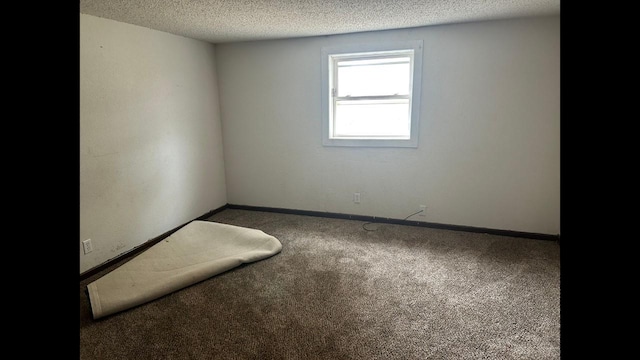 unfurnished room with a textured ceiling, dark colored carpet, and baseboards