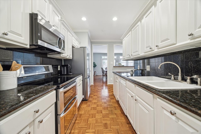 kitchen featuring crown molding, appliances with stainless steel finishes, white cabinets, a sink, and dark stone countertops