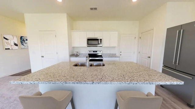 kitchen featuring stainless steel appliances, a kitchen island with sink, white cabinetry, and a kitchen bar