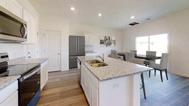 kitchen featuring stainless steel appliances, a sink, light wood-style floors, white cabinets, and a center island with sink