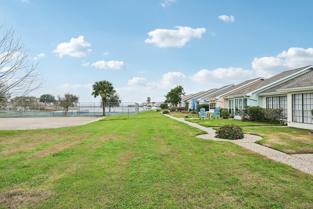 exterior space with a tennis court, fence, and a lawn