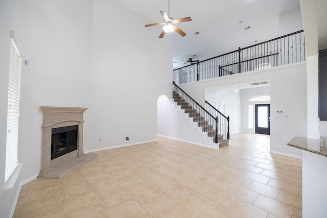 unfurnished living room with a fireplace with raised hearth, visible vents, a towering ceiling, baseboards, and stairway