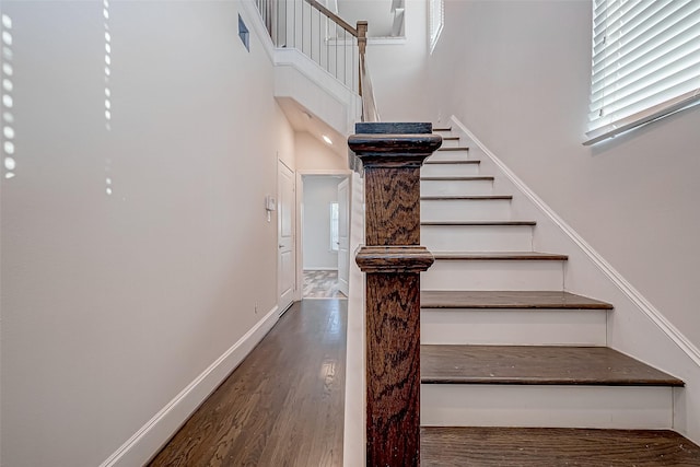 staircase featuring a towering ceiling, baseboards, and wood finished floors