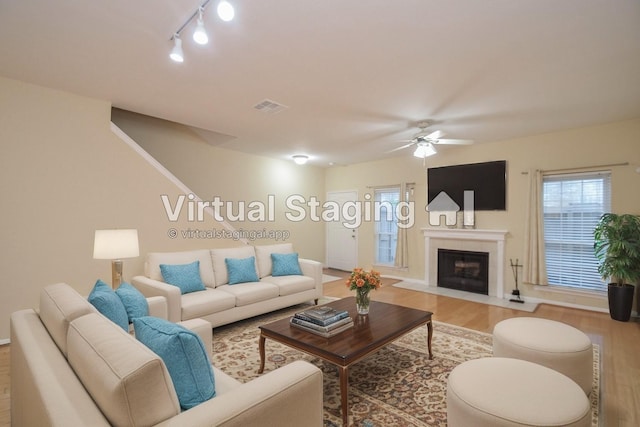 living area featuring baseboards, visible vents, a fireplace with flush hearth, ceiling fan, and wood finished floors