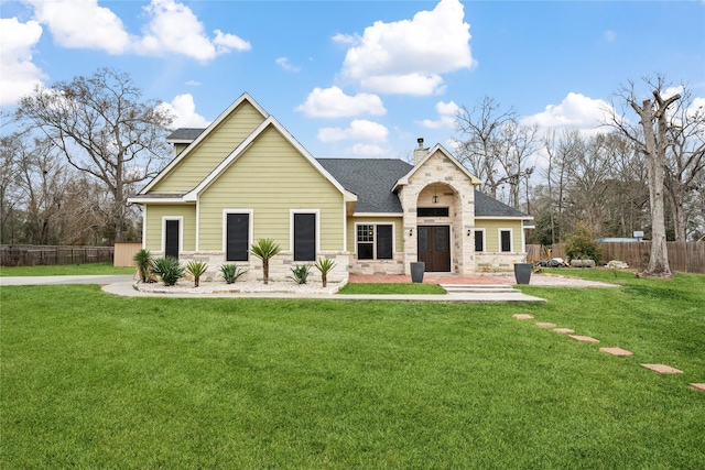 view of front of home with stone siding, a chimney, roof with shingles, fence, and a front yard