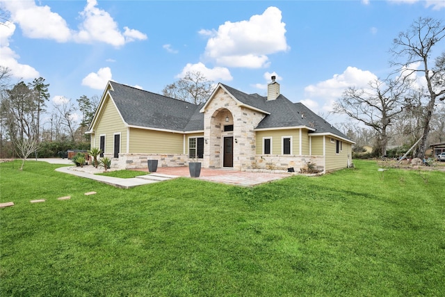 back of house featuring a patio, a yard, a chimney, and stone siding